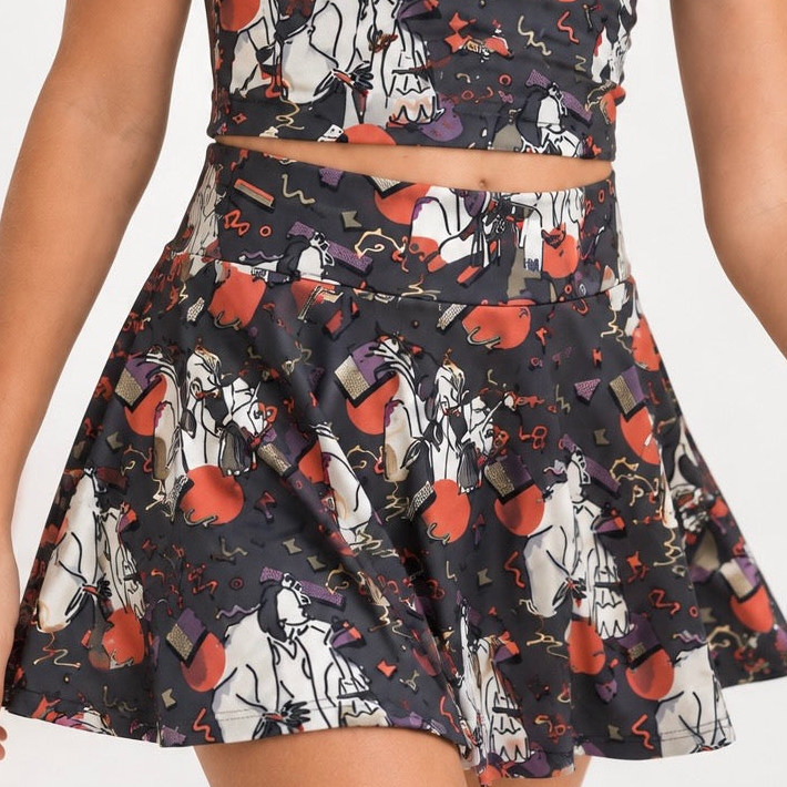 A child wearing a sleeveless two-piece outfit with a matching crop top and flared skirt, featuring a Halloween-themed print of ghosts, pumpkins, and candy on a dark background.